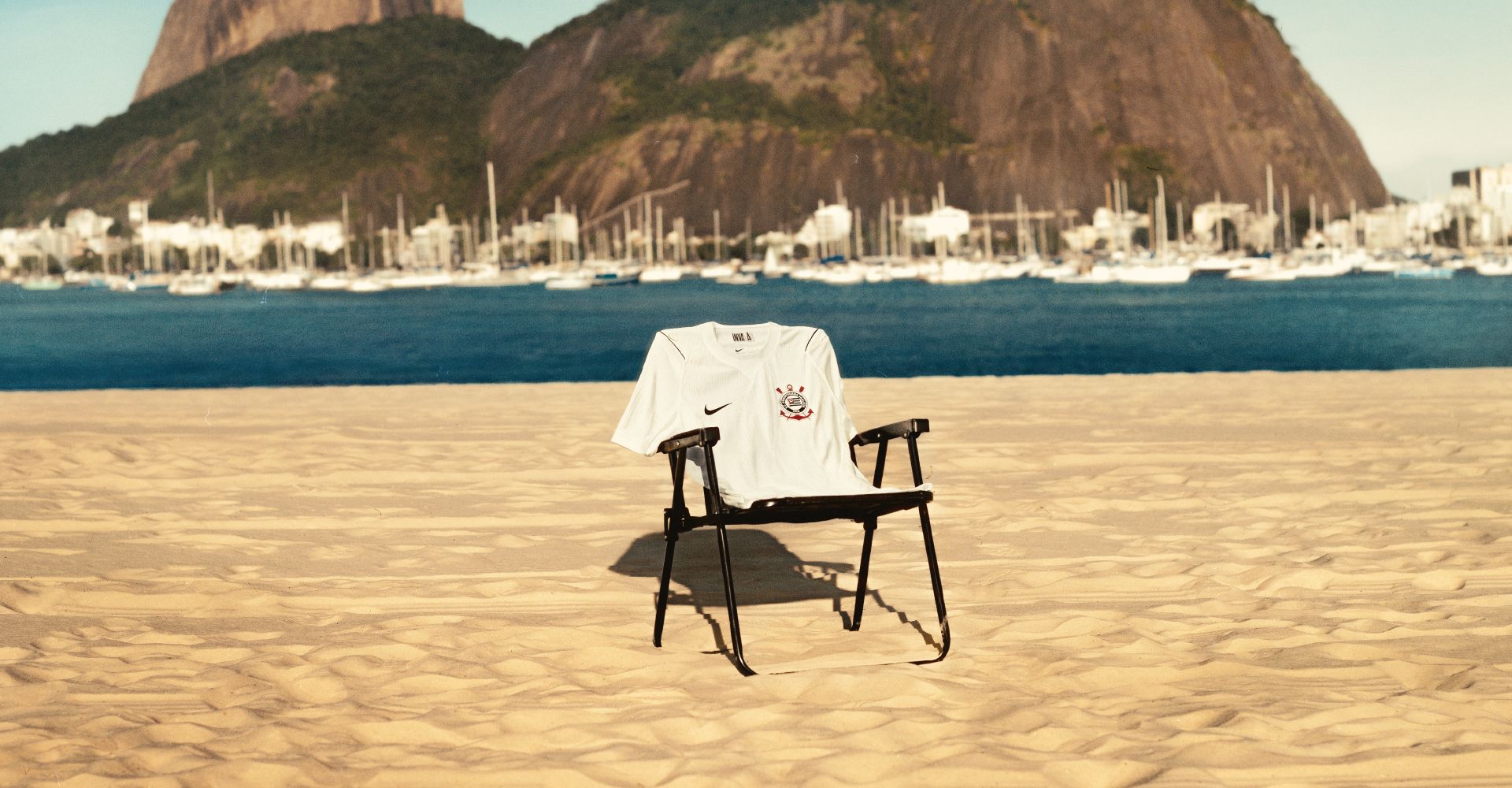 Nova camisa da Coleção Corinthians 50 anos pendurada em uma cadeira no meio da praia, com o mar no fundo