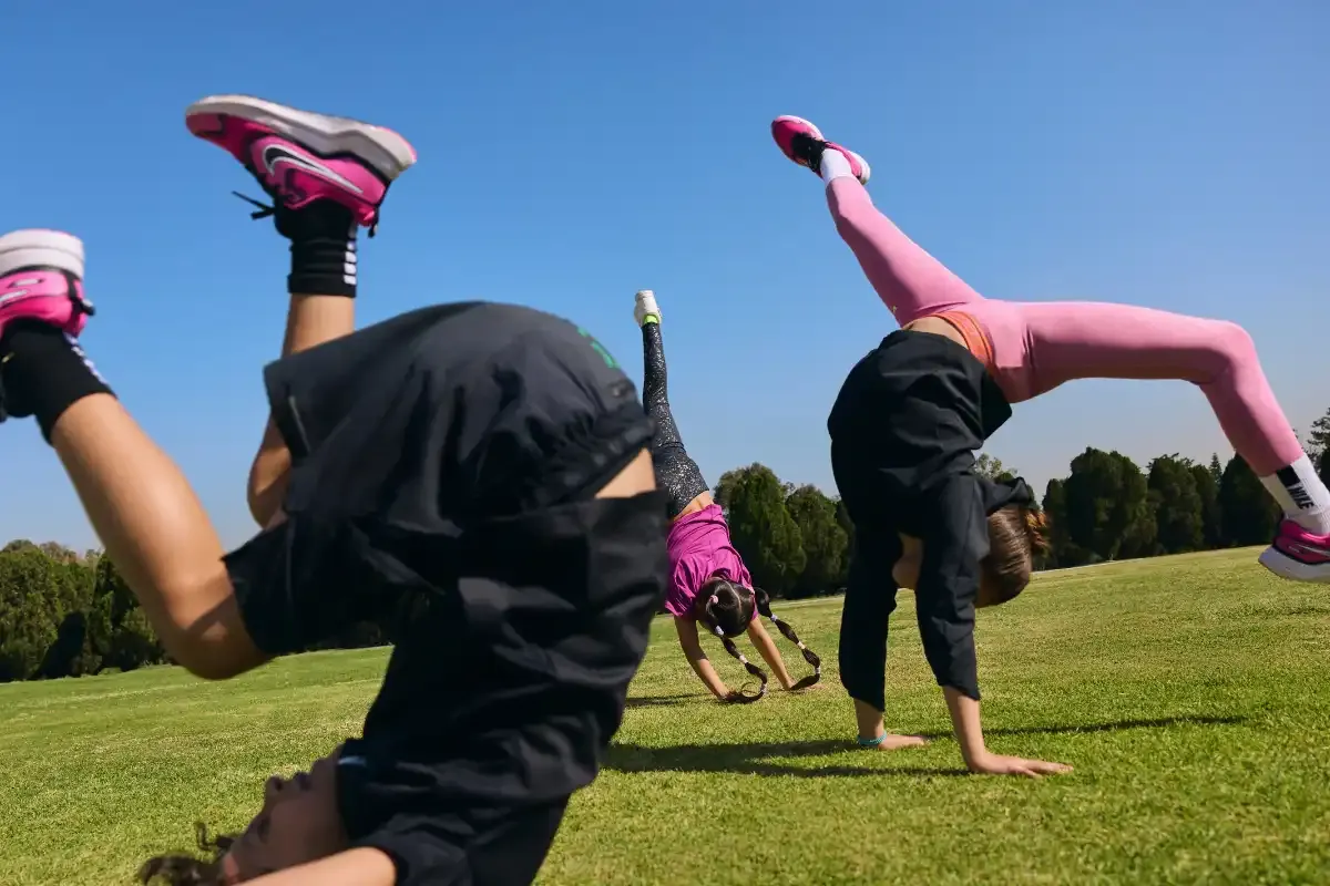 Crianças praticando exercícios ao ar livre em um campo verde sob céu claro, com árvores ao fundo.