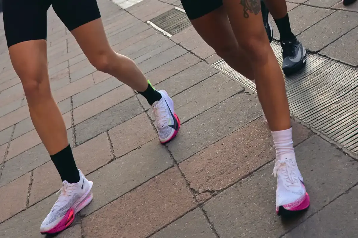 Duas mulheres praticando corrida ao ar livre na cidade, focadas em seus tênis de corrida modernos, roupas esportivas confortáveis e amarradas.