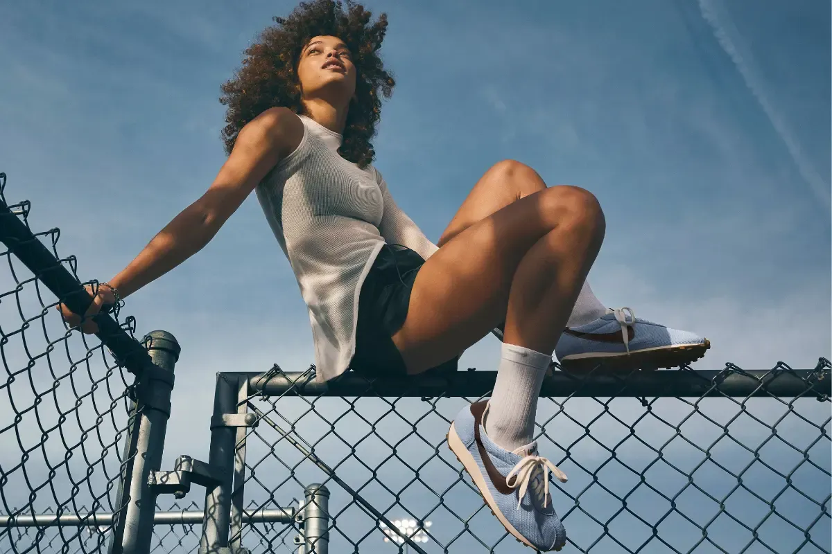 Mulher com roupa esportiva sentada em cerca de quadra usando tênis Nike