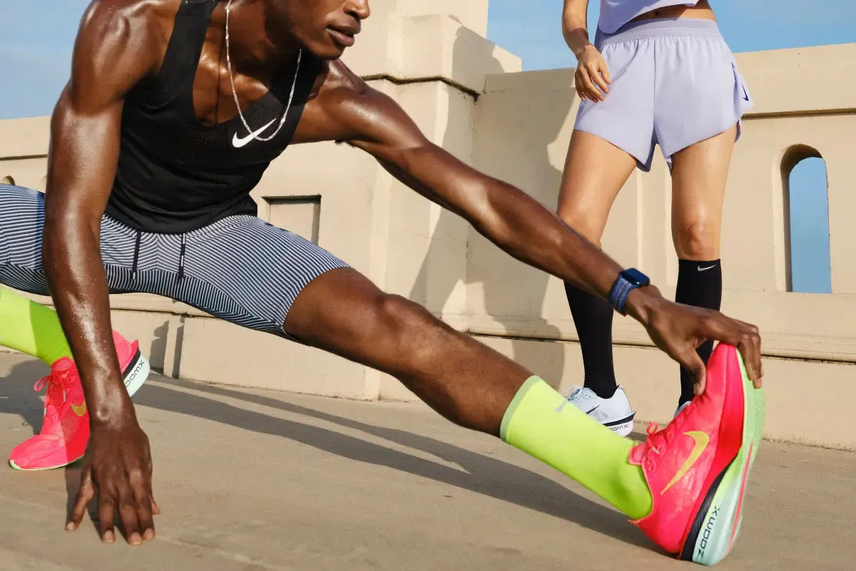 Atleta fazendo alongamento antes da corrida usando tênis esportivo Nike em área externa.