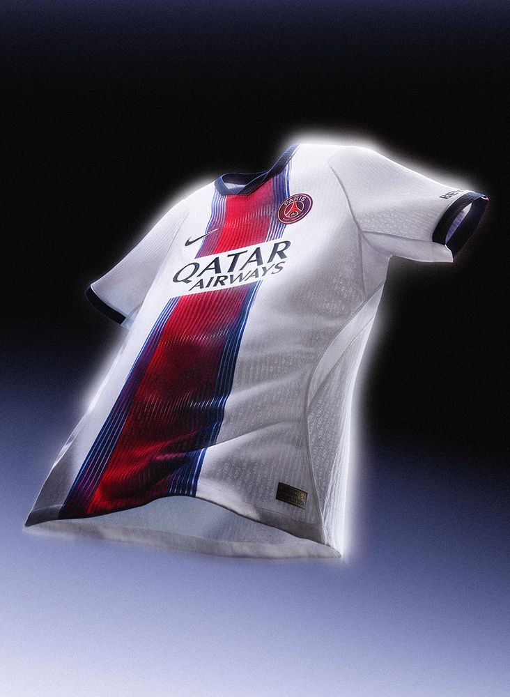 Uma camisa branca de futebol do Paris Saint-Germain flutuando contra um fundo escuro, com uma faixa central vermelha e azul.