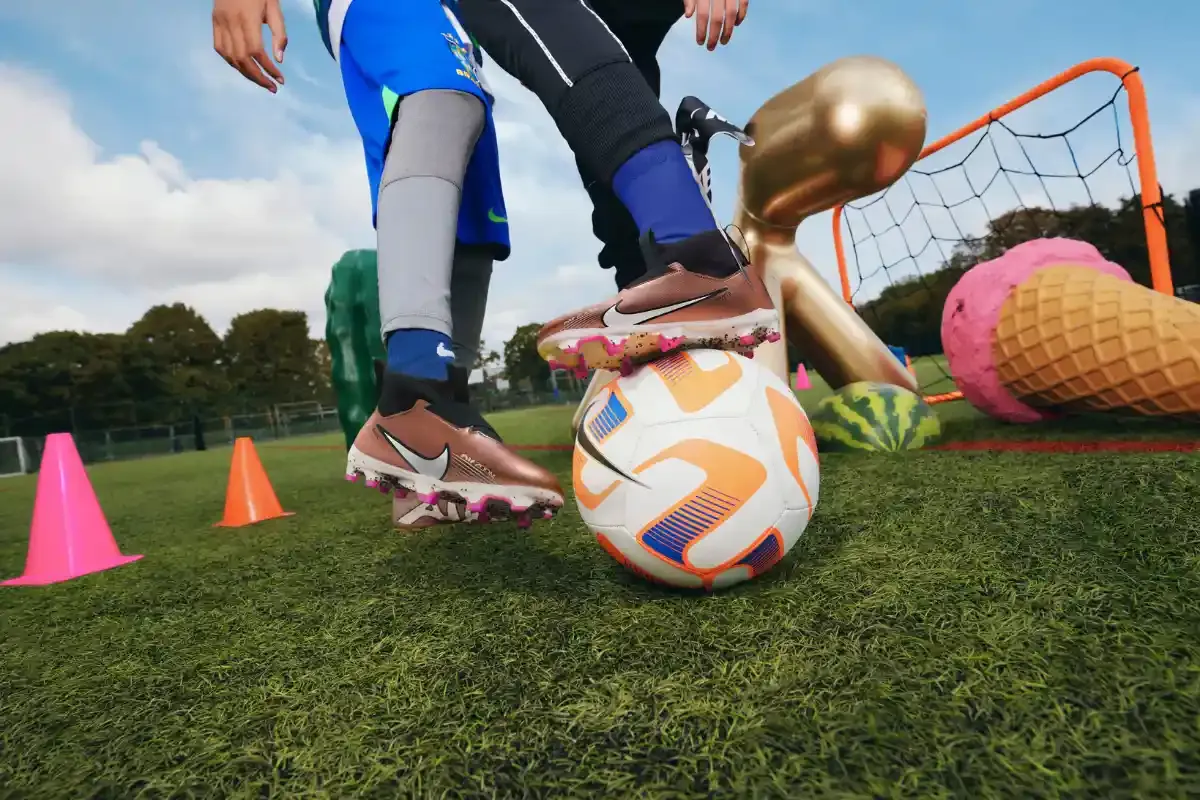 Imagem de uma criança praticando futebol infantil ao ar livre, com bolas, cones de treino e gol de tamanho pequeno, em campo gramado.