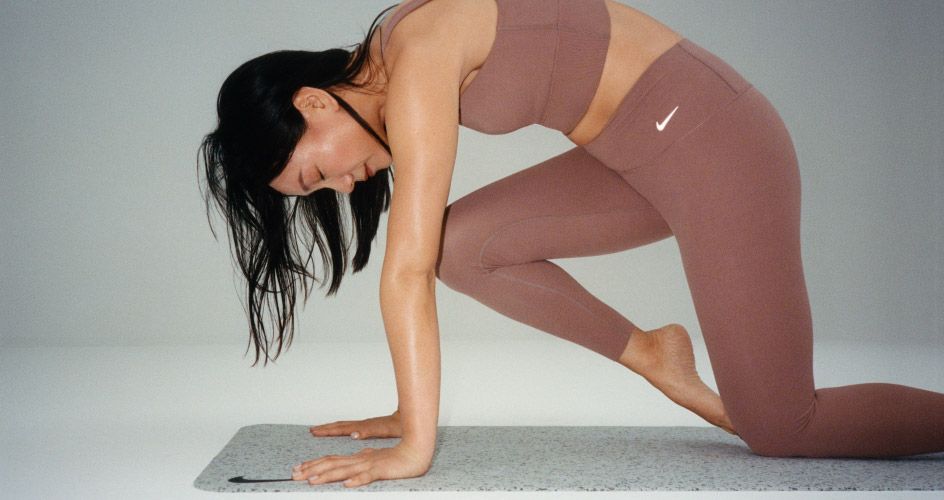 Mulher se exercitando no tapete de yoga com conjunto da Nike marrom.