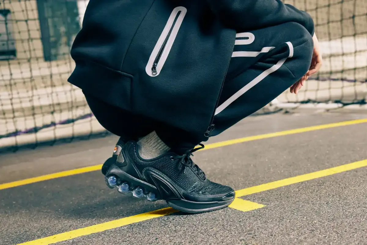 Pessoa agachada com calçados esportivos de corrida e roupas de esportes em uma quadra.