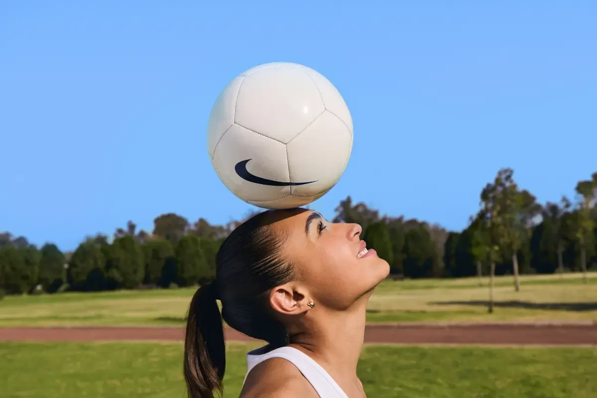 mulher com bola na cabeça enquanto joga futebol