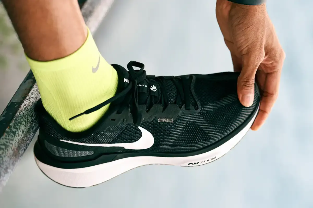Pessoa ajustando tênis de corrida Nike preto e branco enquanto usa meia amarelo durante exercício.