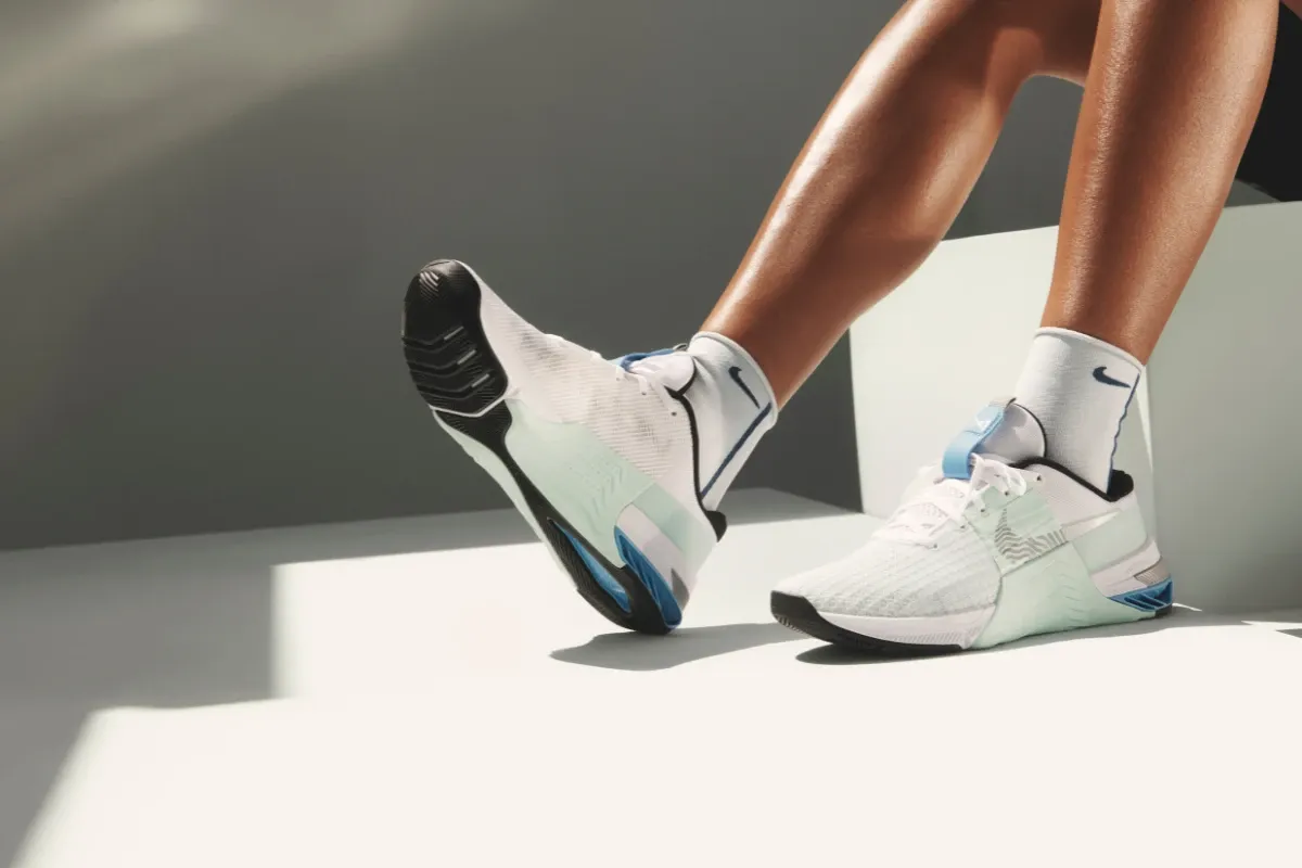 Pessoa usando tênis esportivos Nike em uma superfície branca com sombra ao lado.