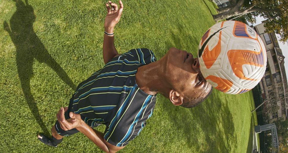 Homem equilibrando a bola de futebol na testa.